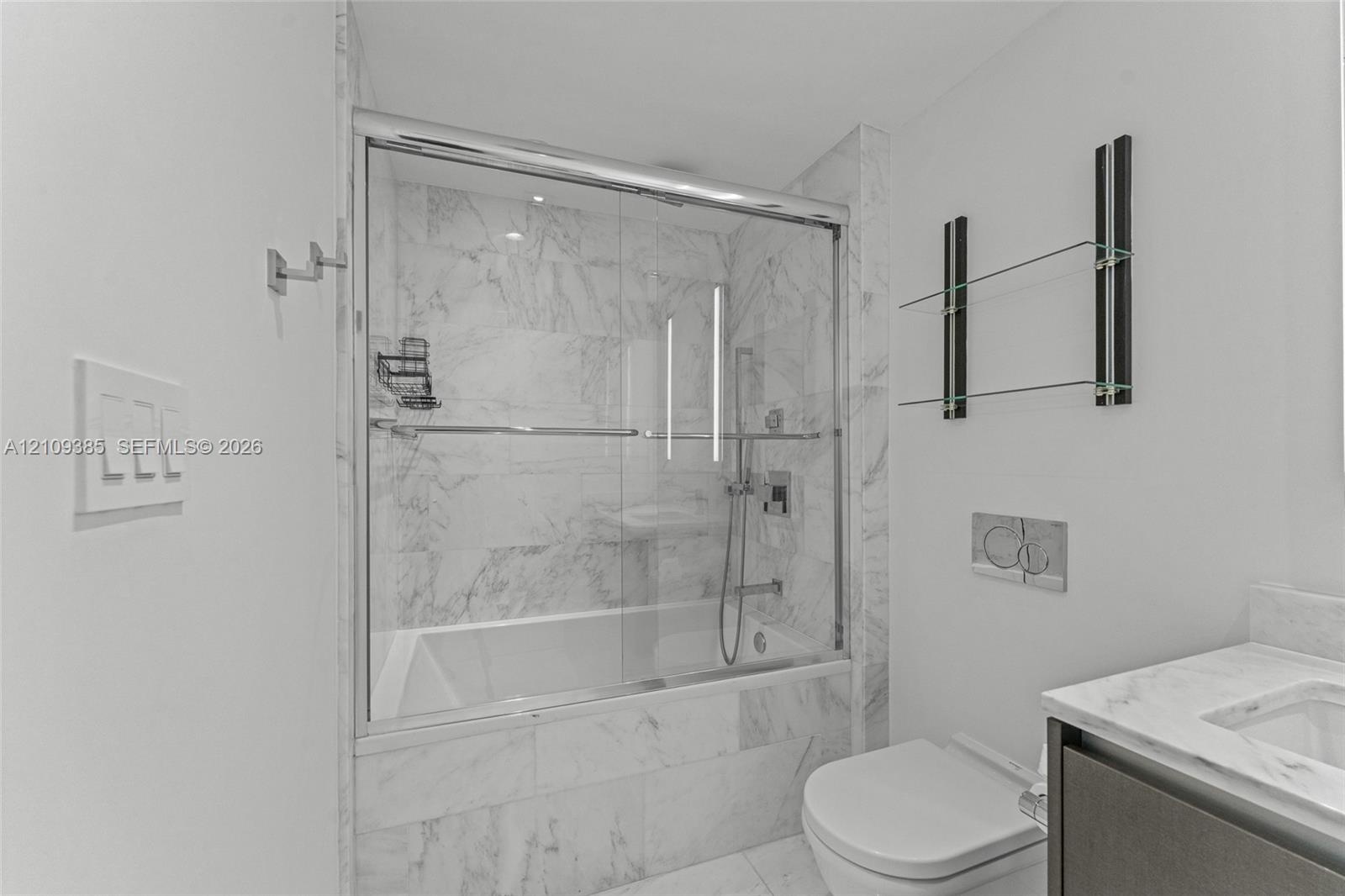 Bathroom featuring a tub-shower combination with glass sliding doors, floor-to-ceiling stone-look tiling, a wall-mounted toilet with a dual-flush actu