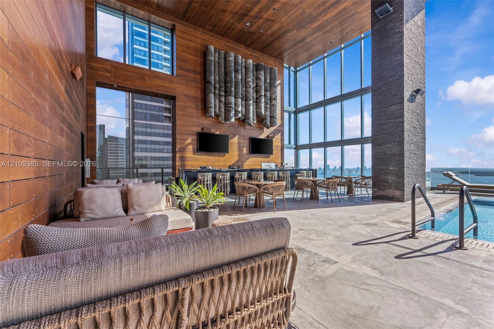 Outdoor lounge featuring wood-paneled walls and ceiling, floor-to-ceiling glass windows, stone-tiled flooring, and a recessed swimming pool with metal
