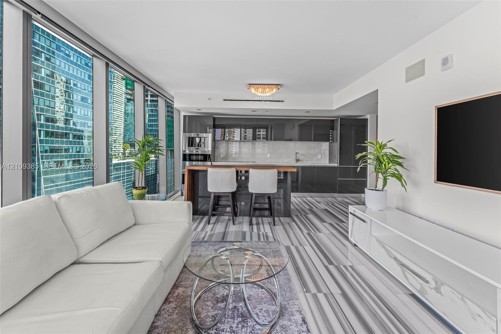 Floor-to-ceiling windows, high-gloss cabinetry, stone-patterned tile flooring, integrated kitchen appliances, and a kitchen island with a wood-finish 