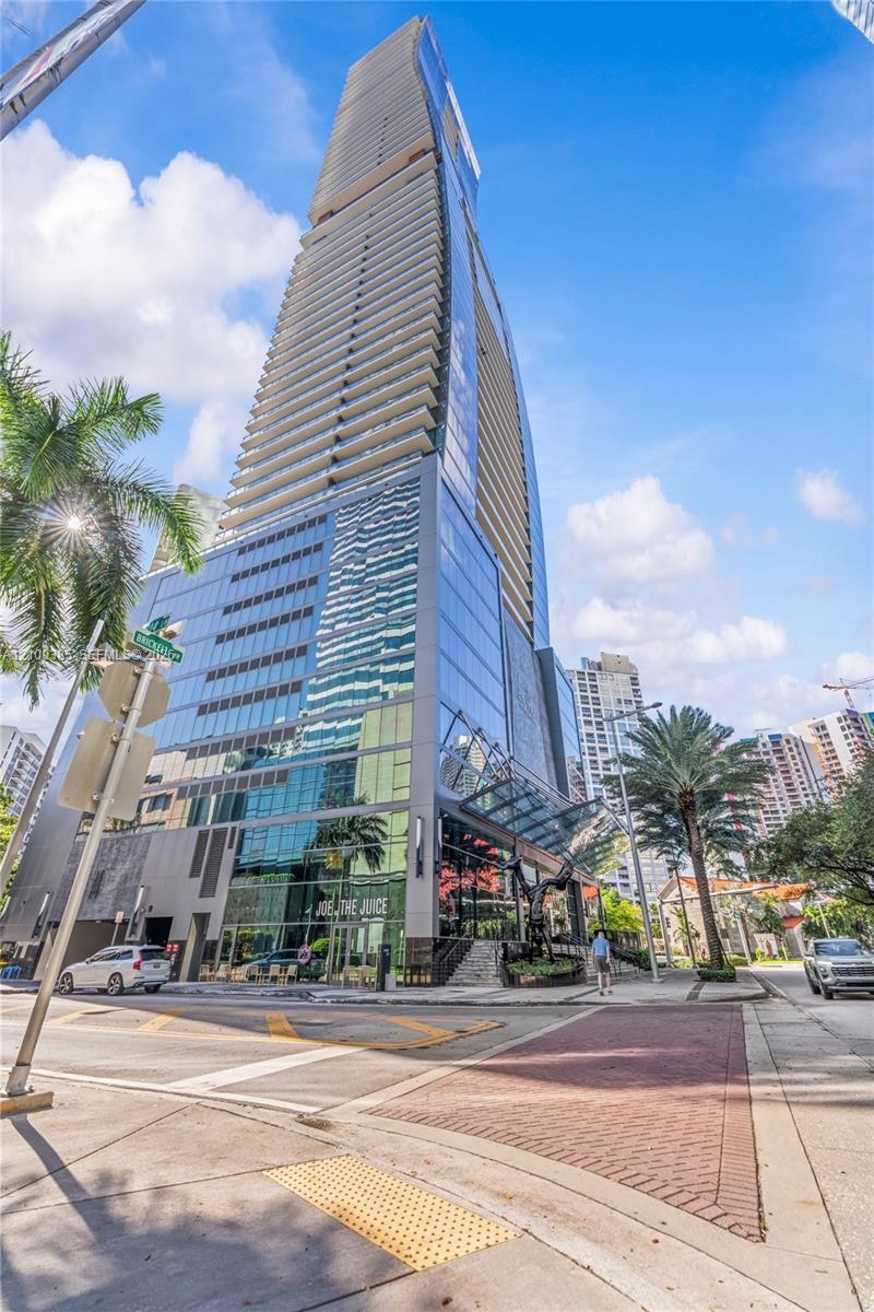 High-rise architectural exterior featuring a glass curtain wall facade, tiered wrap-around balconies, and a prominent glass-canopy entryway