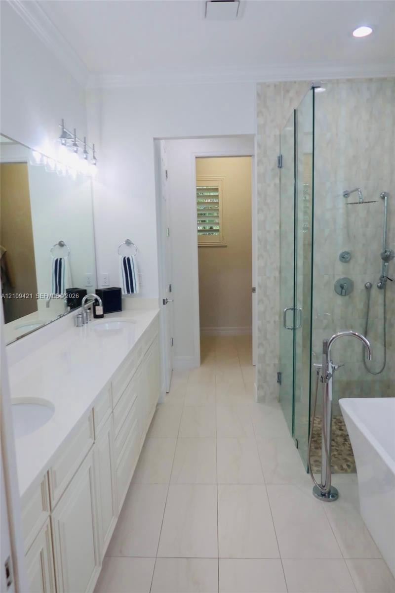 Dual-sink vanity with a solid-surface countertop, glass-enclosed walk-in shower with multi-head fixtures, freestanding soaking tub with floor-mounted 