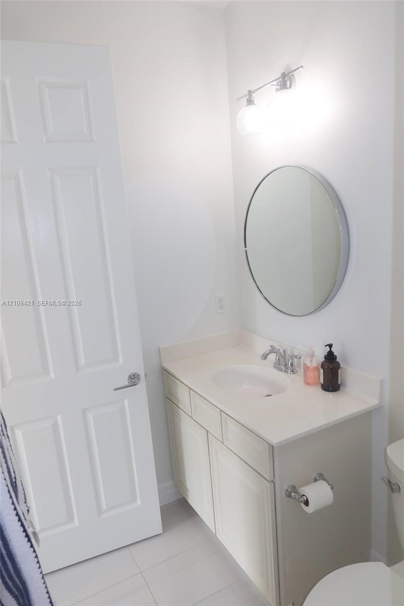 Bathroom featuring a vanity with a white solid-surface countertop, an integrated sink, polished chrome faucet, circular wall mirror, and dual-bulb van