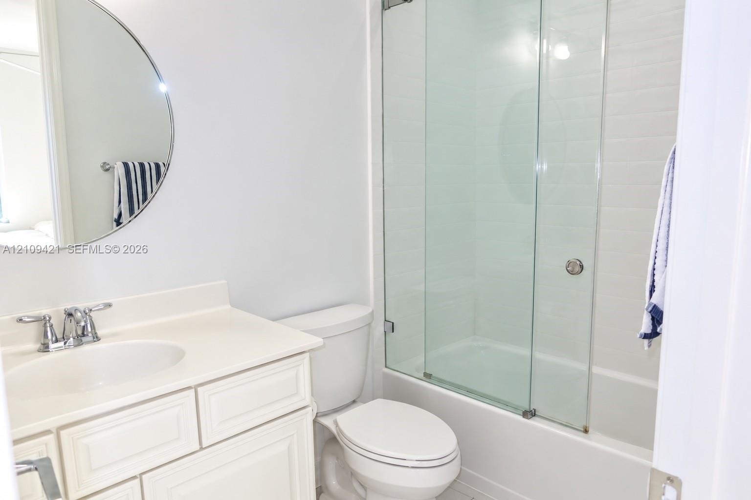 Bathroom featuring a vanity with an integrated sink and chrome faucet, circular wall mirror, and a tub-shower combination enclosed by sliding glass do