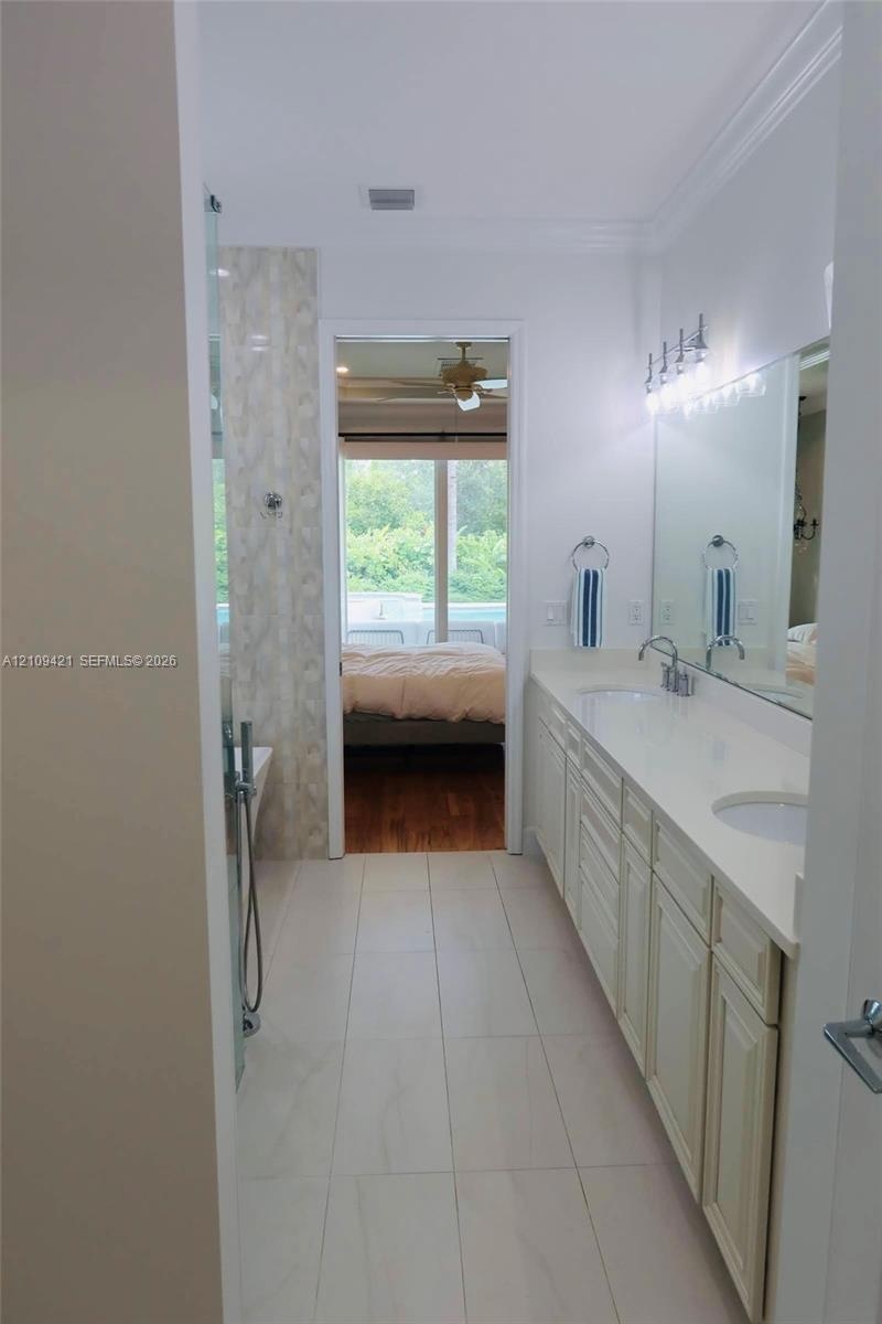 Bathroom featuring dual-sink vanity with light-tone cabinetry, quartz countertop, full-width wall mirror, and large-format tile flooring
