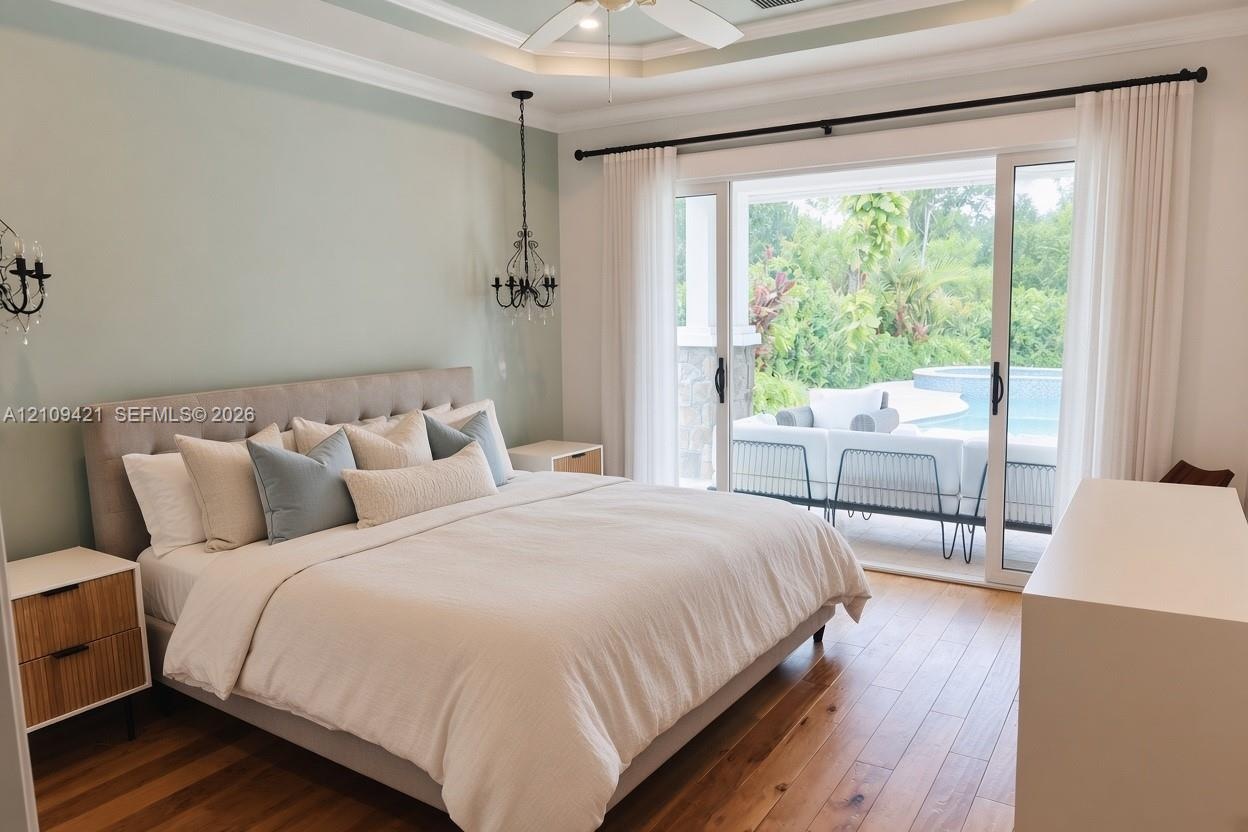 Tray ceiling with crown molding, wood-finish flooring, dual metal-and-crystal chandeliers, and sliding glass doors