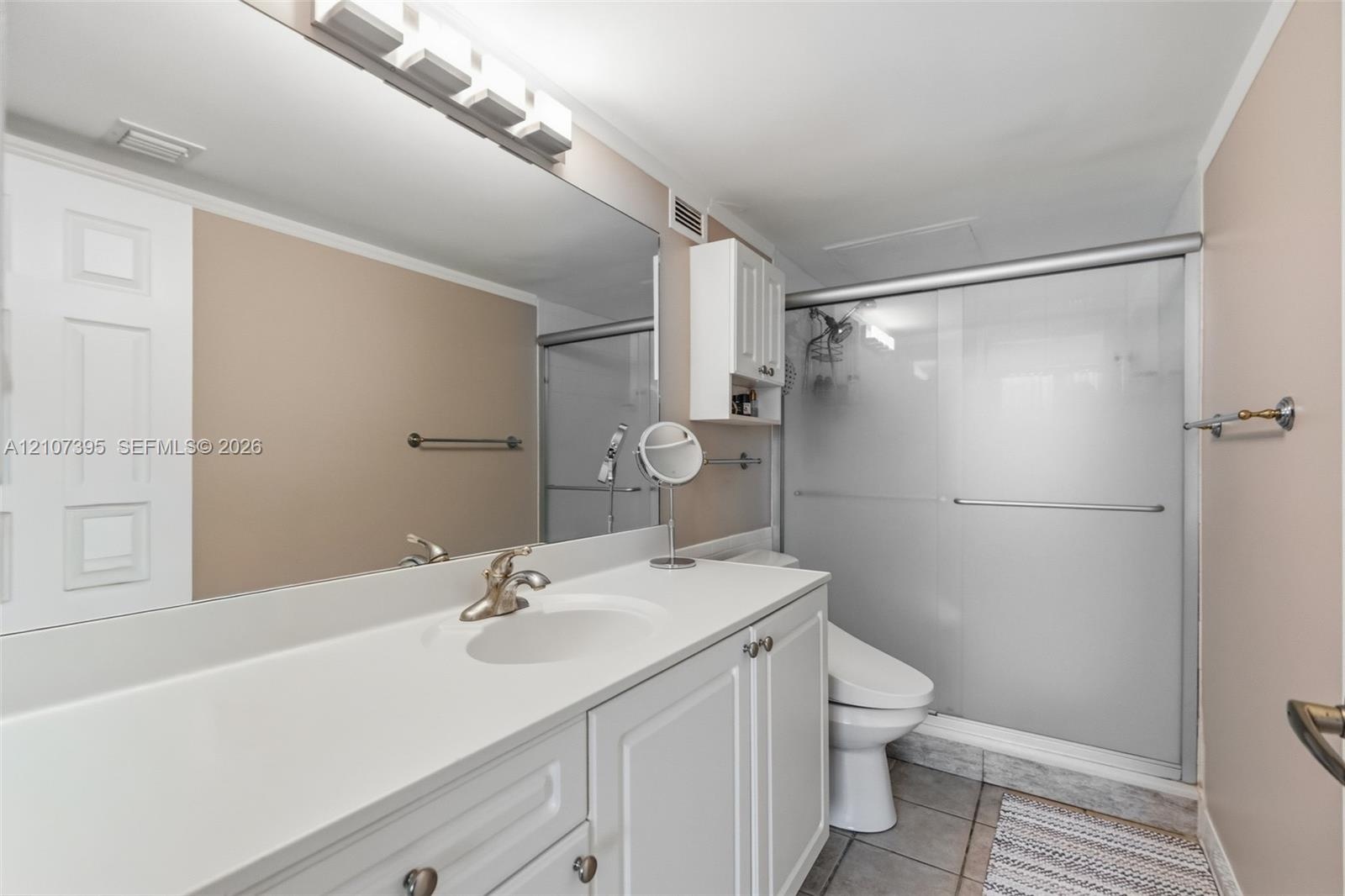 Bathroom featuring a white vanity with an integrated basin, a full-width wall mirror, an overhead multi-light fixture, built-in upper cabinetry, and a