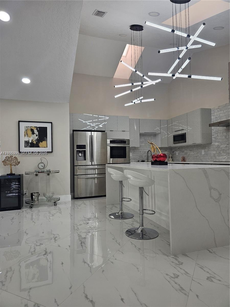 Modern kitchen featuring a waterfall island with stone-finish countertops, high-gloss cabinetry, stainless steel appliances, large-format tile floorin