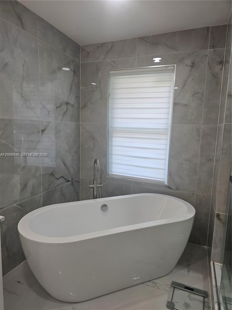 Freestanding soaking tub featuring a chrome floor-mounted faucet and large-format porcelain wall tile with a neutral-toned veined pattern