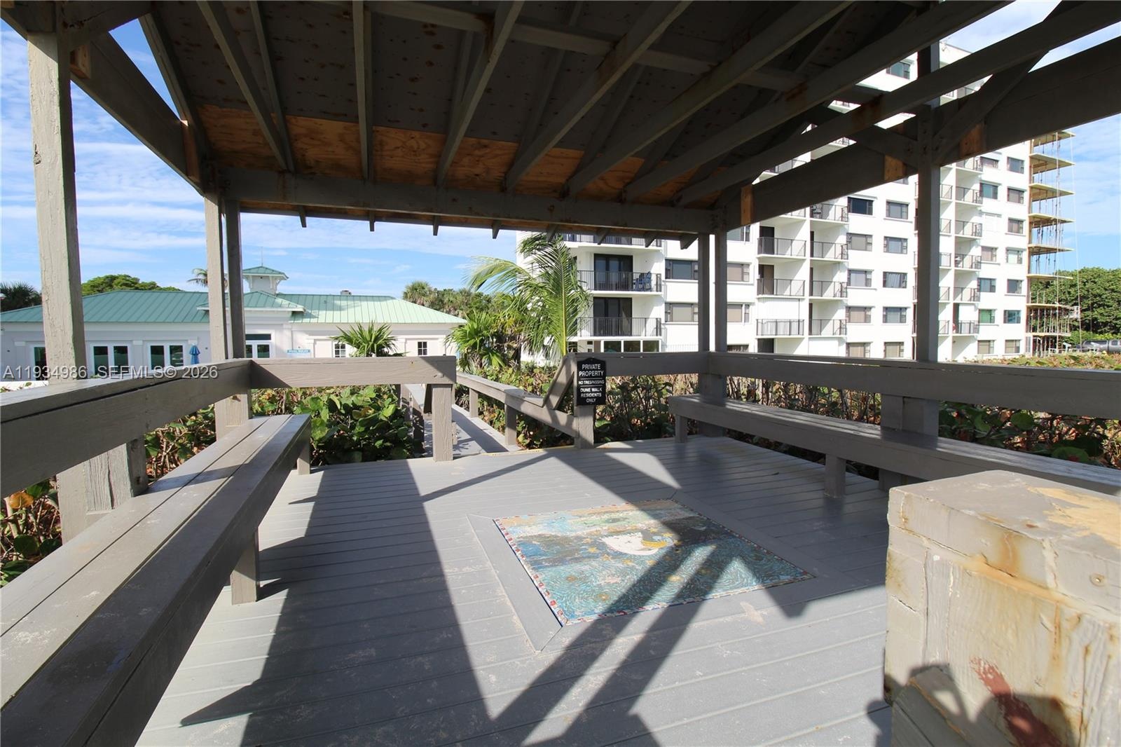 Covered wooden gazebo featuring built-in bench seating, plank flooring, and a decorative tile inlay