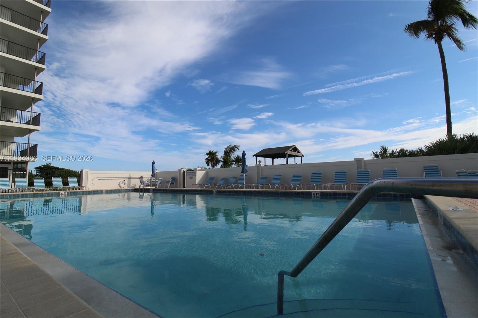 In-ground swimming pool with tile surround, concrete decking, metal safety handrails, and perimeter privacy wall