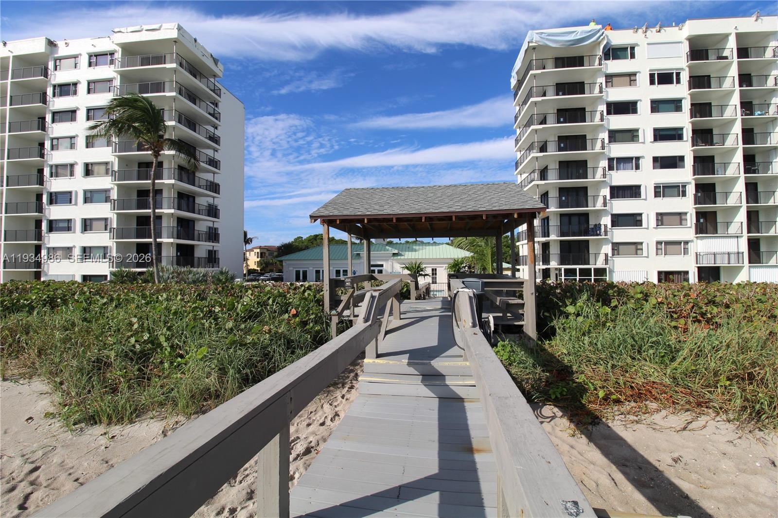 Elevated wooden boardwalk featuring a covered gazebo, built-in benches, and direct path toward multi-story residential buildings