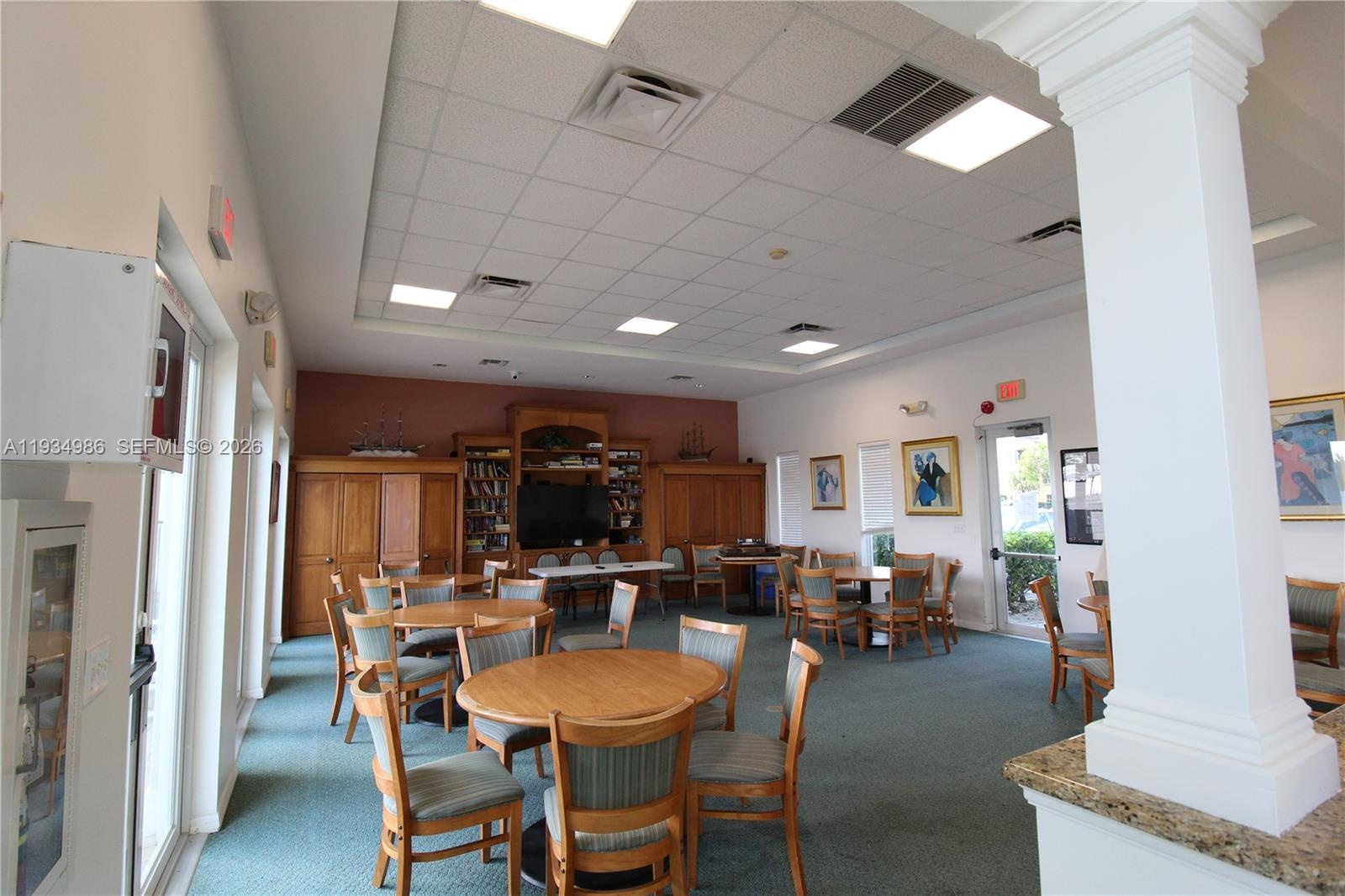 Open-concept common area featuring a dropped tile ceiling with recessed lighting, integrated wood cabinetry, a decorative column, and natural stone-su