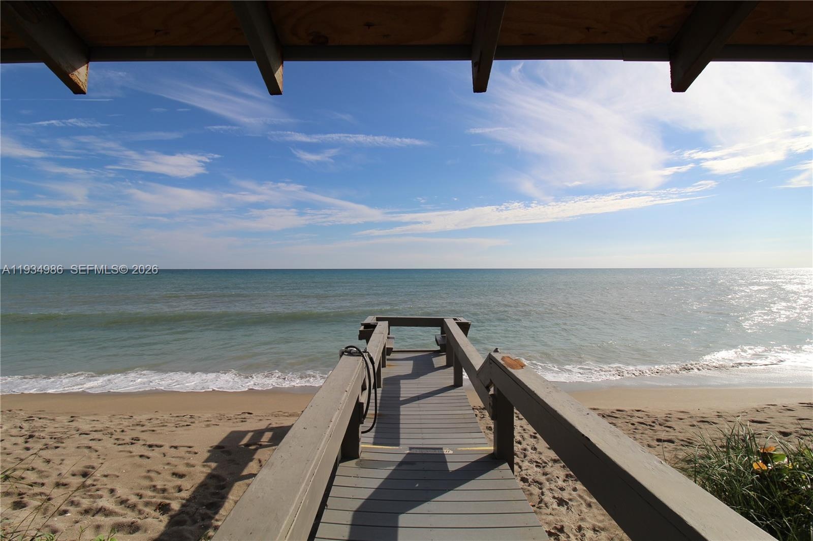 Covered wooden deck featuring a direct staircase leading to a private sandy beach