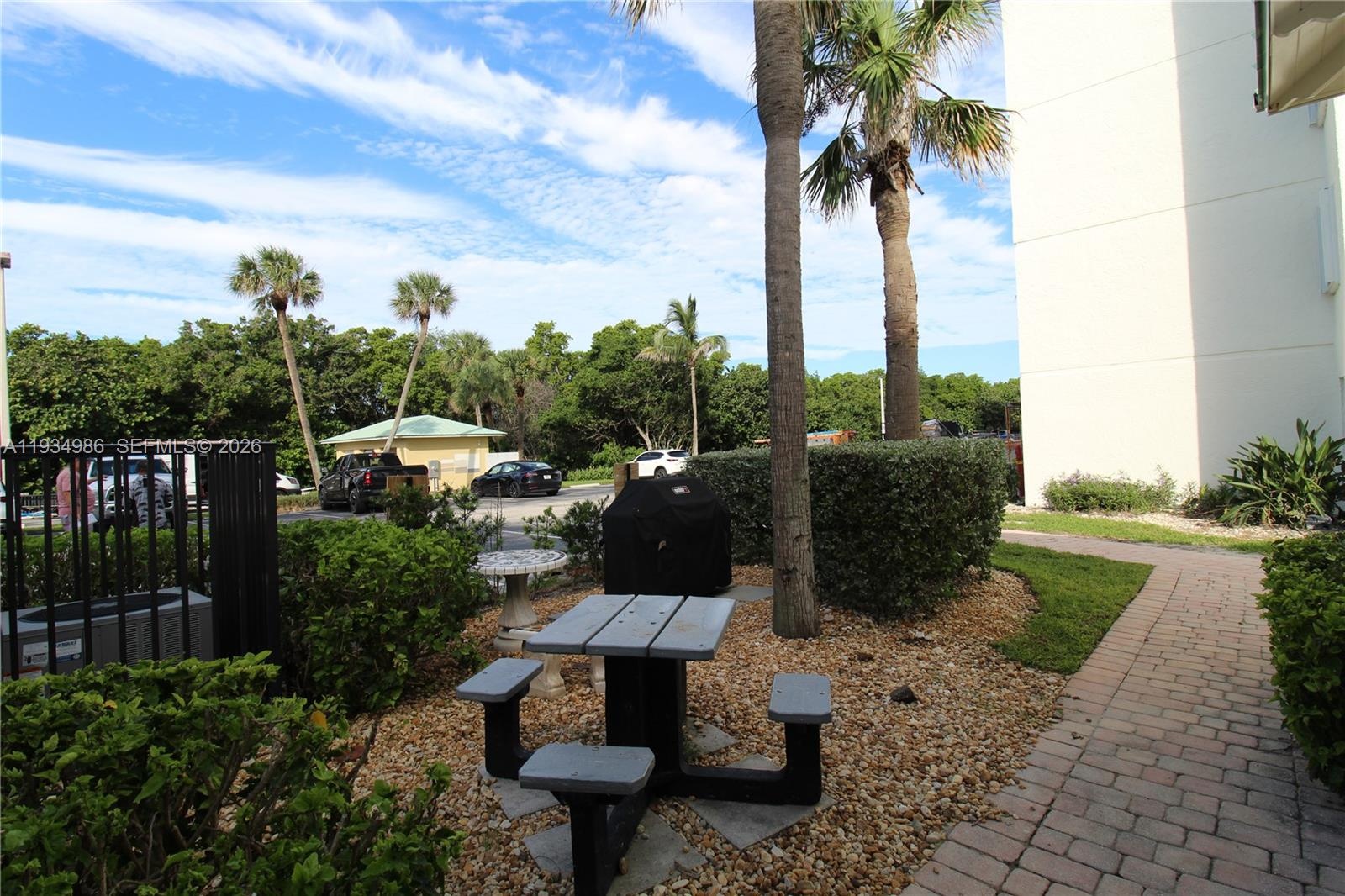 Exterior ground featuring a paved stone walkway, mature palm trees, landscaped shrubbery, and gravel surfacing