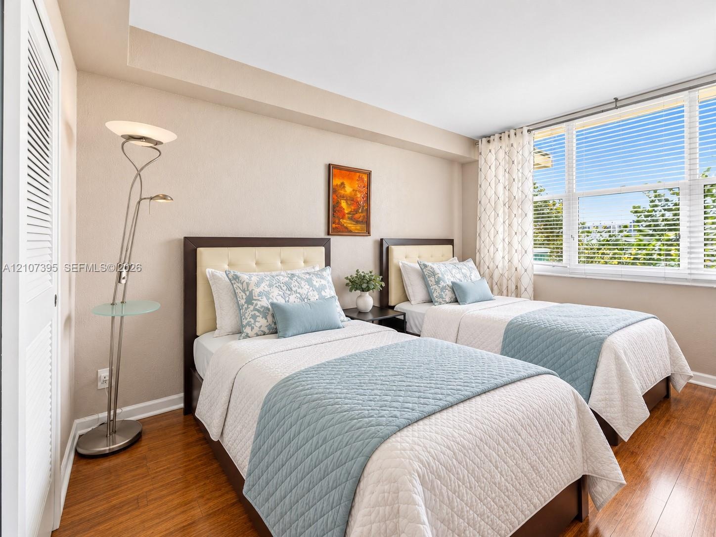 Bedroom featuring wood-finish flooring, recessed ceiling detail, and large windows with horizontal blinds