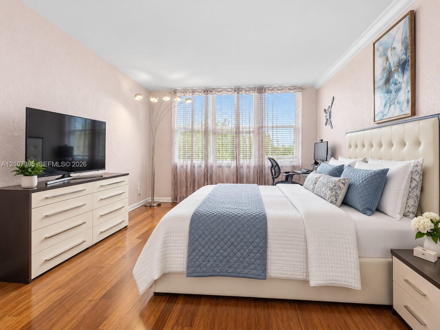 Room interior featuring wood-finish flooring, crown molding, and large window banks with horizontal blinds