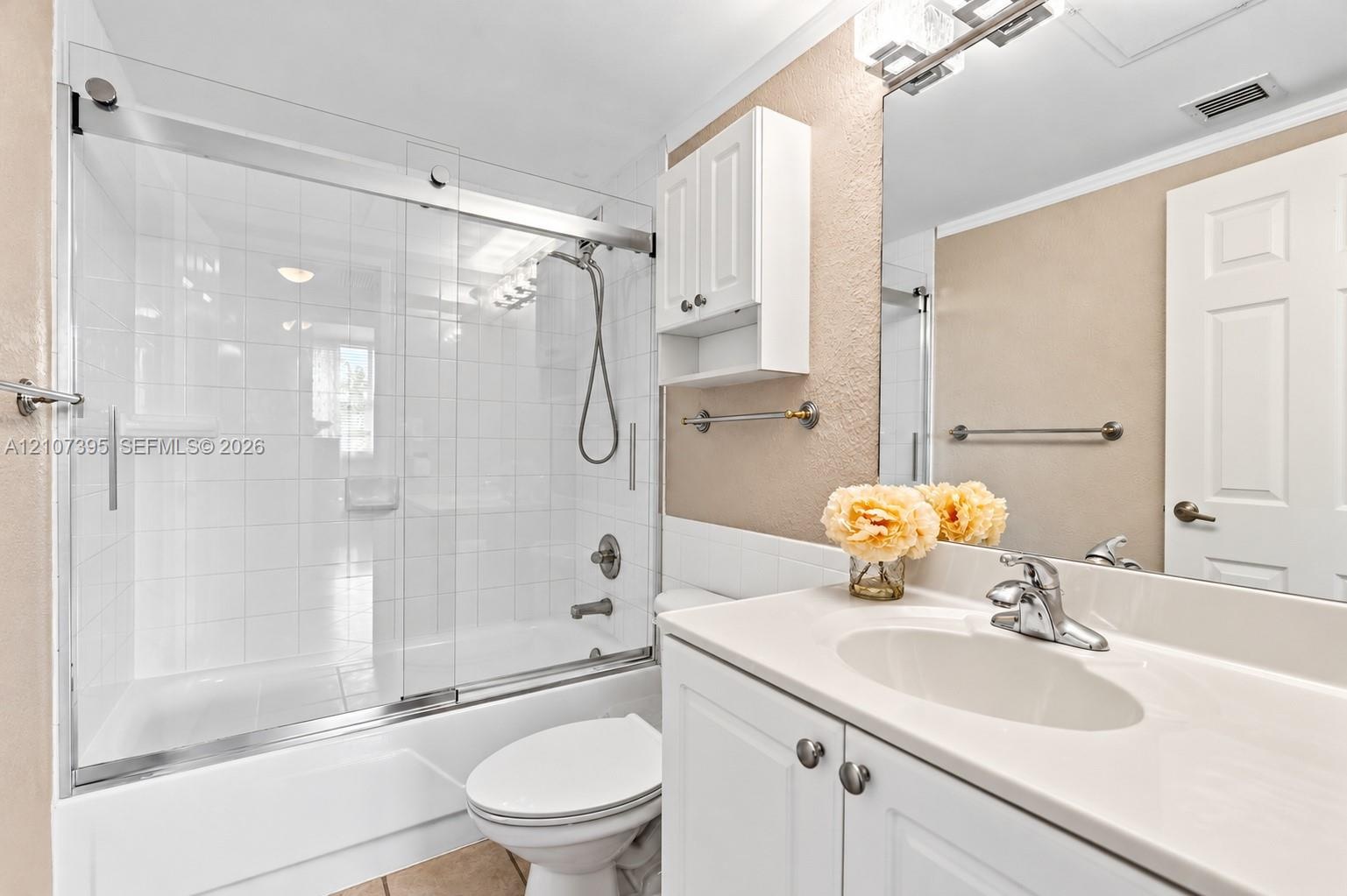 Bathroom featuring a white vanity cabinet with an integrated sink, polished chrome faucet, glass-enclosed shower and tub combination with tile surroun