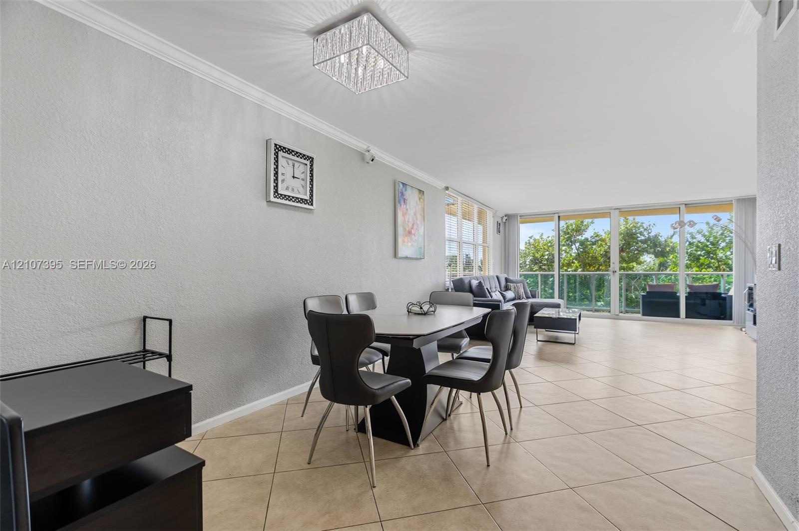 Open-concept interior featuring large-format tile flooring, crown molding, a crystal-accented flush mount light fixture, and floor-to-ceiling glass sl
