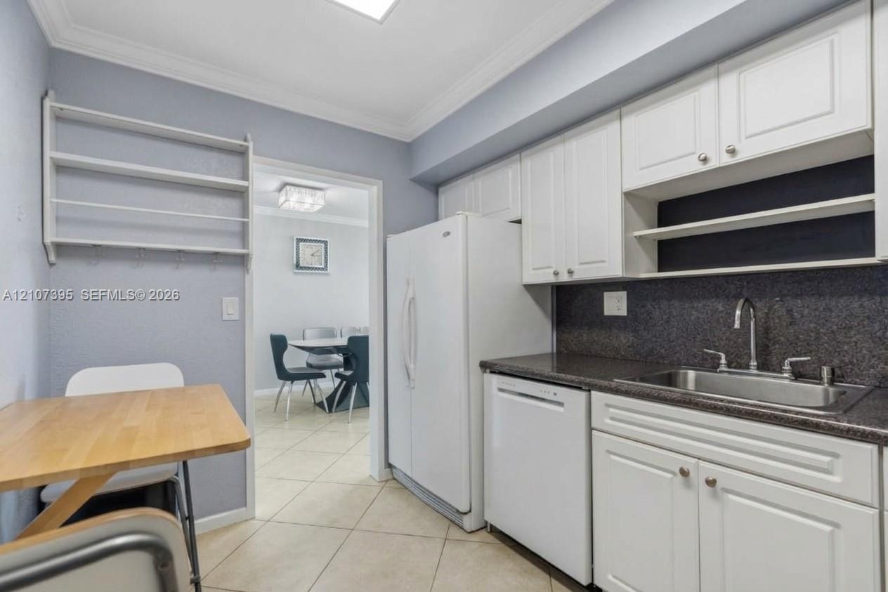 Kitchen featuring white raised-panel cabinetry, dark stone-finish countertops, stainless steel sink with gooseneck faucet, tile flooring, and built-in