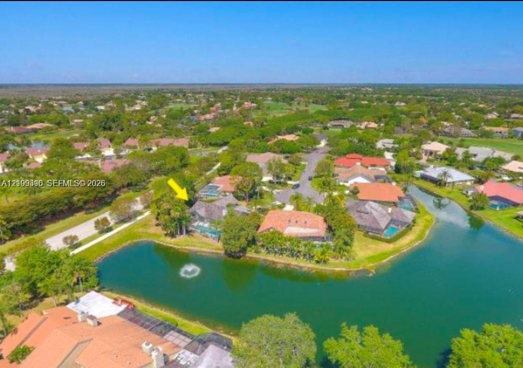 Aerial perspective of a waterfront property featuring a screened-in pool enclosure, tile roofing, and mature perimeter landscaping