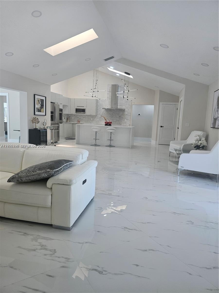 Open-concept interior featuring vaulted ceilings, skylights, large-format tile flooring, recessed lighting, and a kitchen island with a stone-finish b