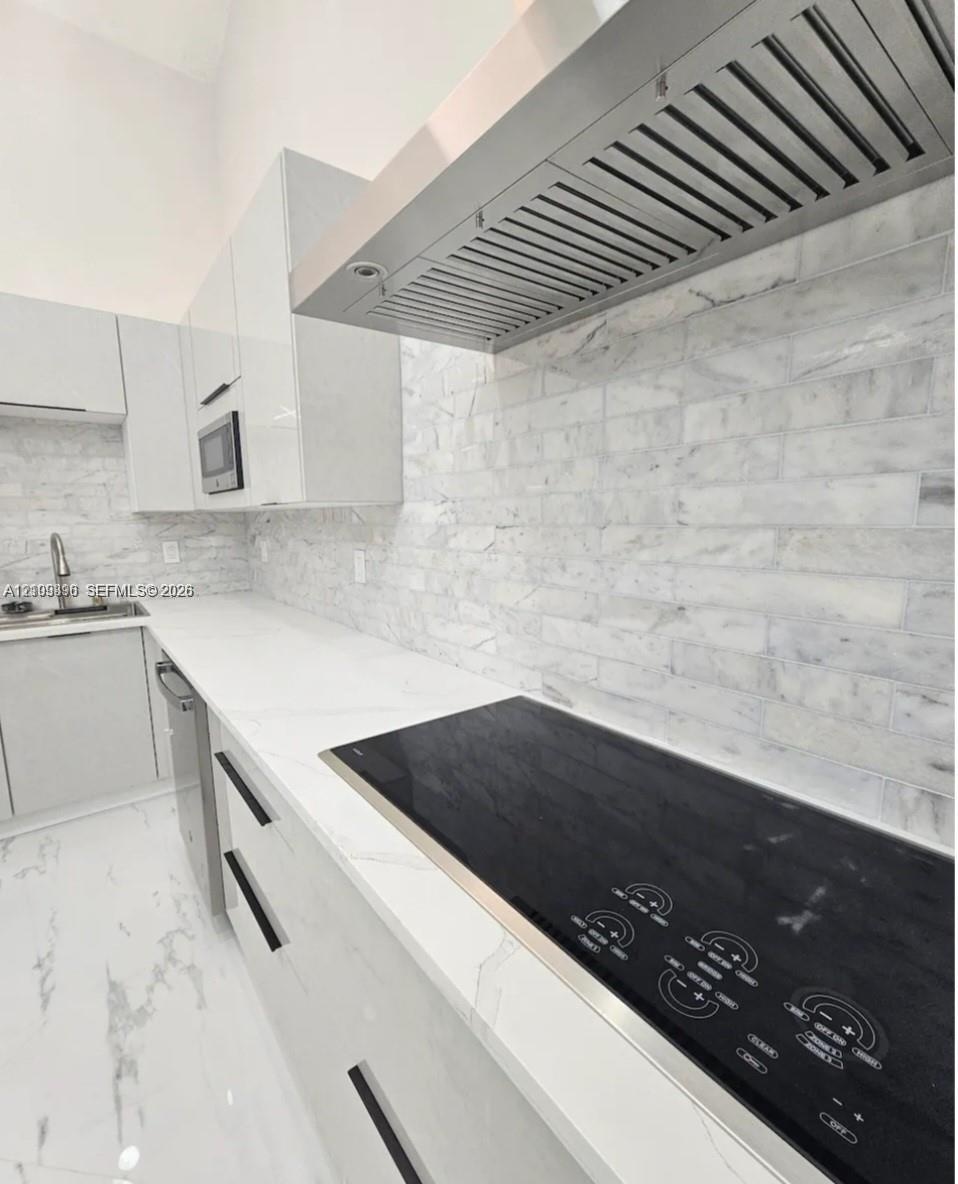 Contemporary kitchen featuring high-gloss cabinetry, stone-finish countertops, subway tile backsplash, a stainless steel range hood, and integrated el