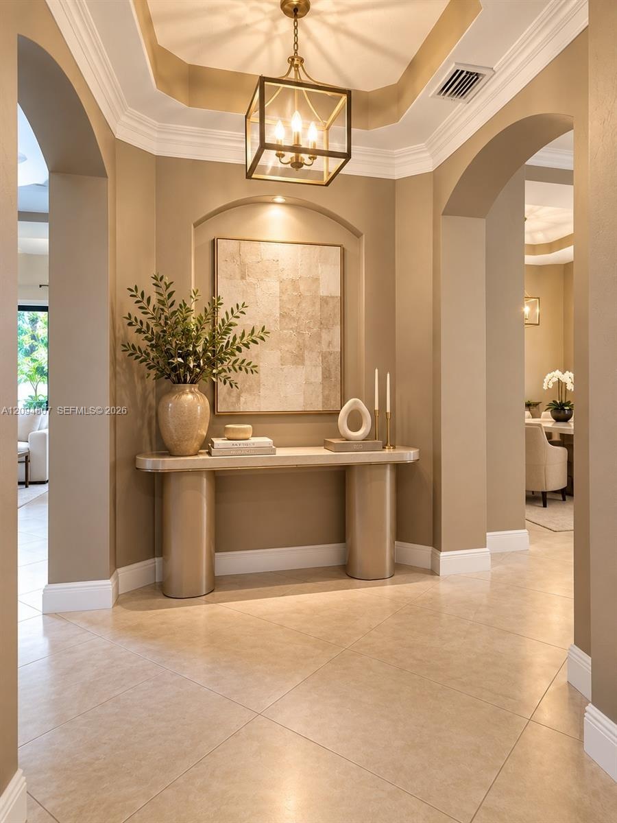 Foyer featuring a recessed tray ceiling, arched passageways, a built-in recessed display niche, and large-format tile flooring