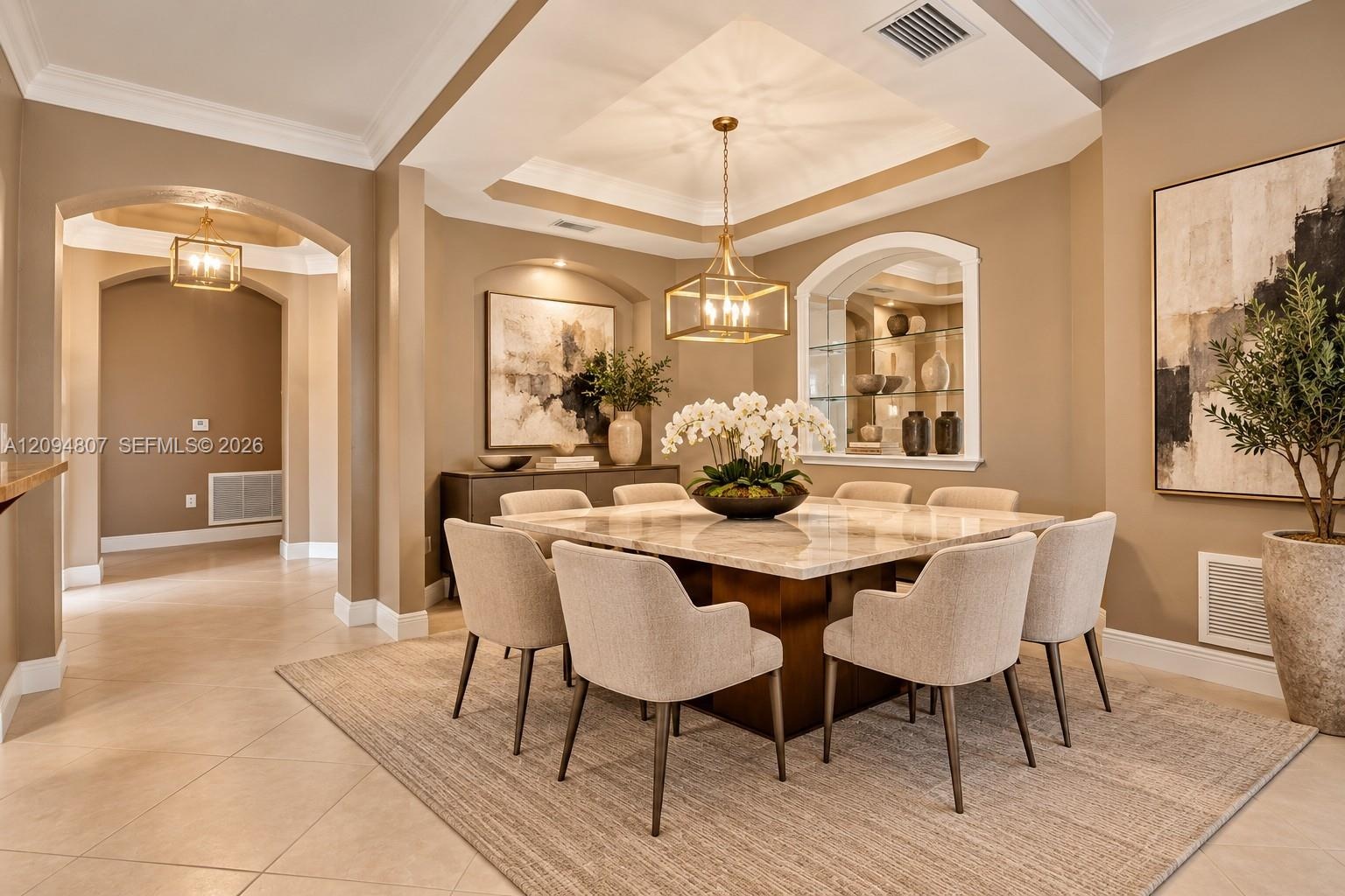 Dining area featuring a tray ceiling, recessed alcove with glass shelving, arched entryways, and crown molding