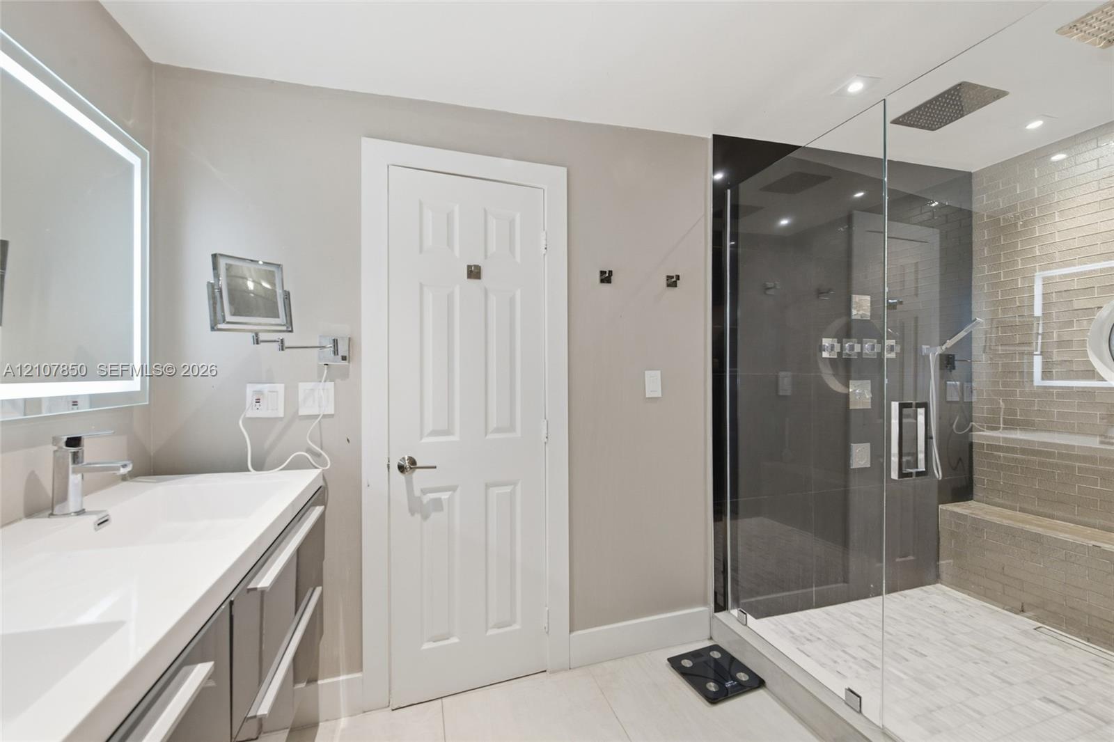 Bathroom featuring a dual-sink vanity with light-toned countertop, walk-in shower with glass enclosure, integrated bench seating, and recessed ceiling