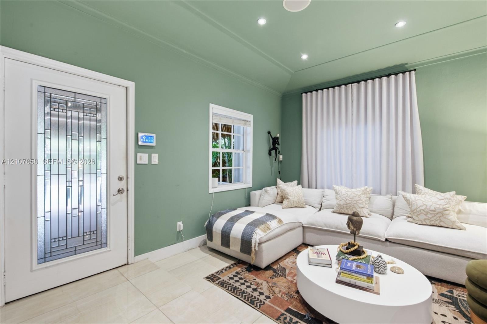 Entry area featuring a glass-inset door with geometric detailing, recessed ceiling lighting, tray ceiling architecture, large-format tile flooring, an