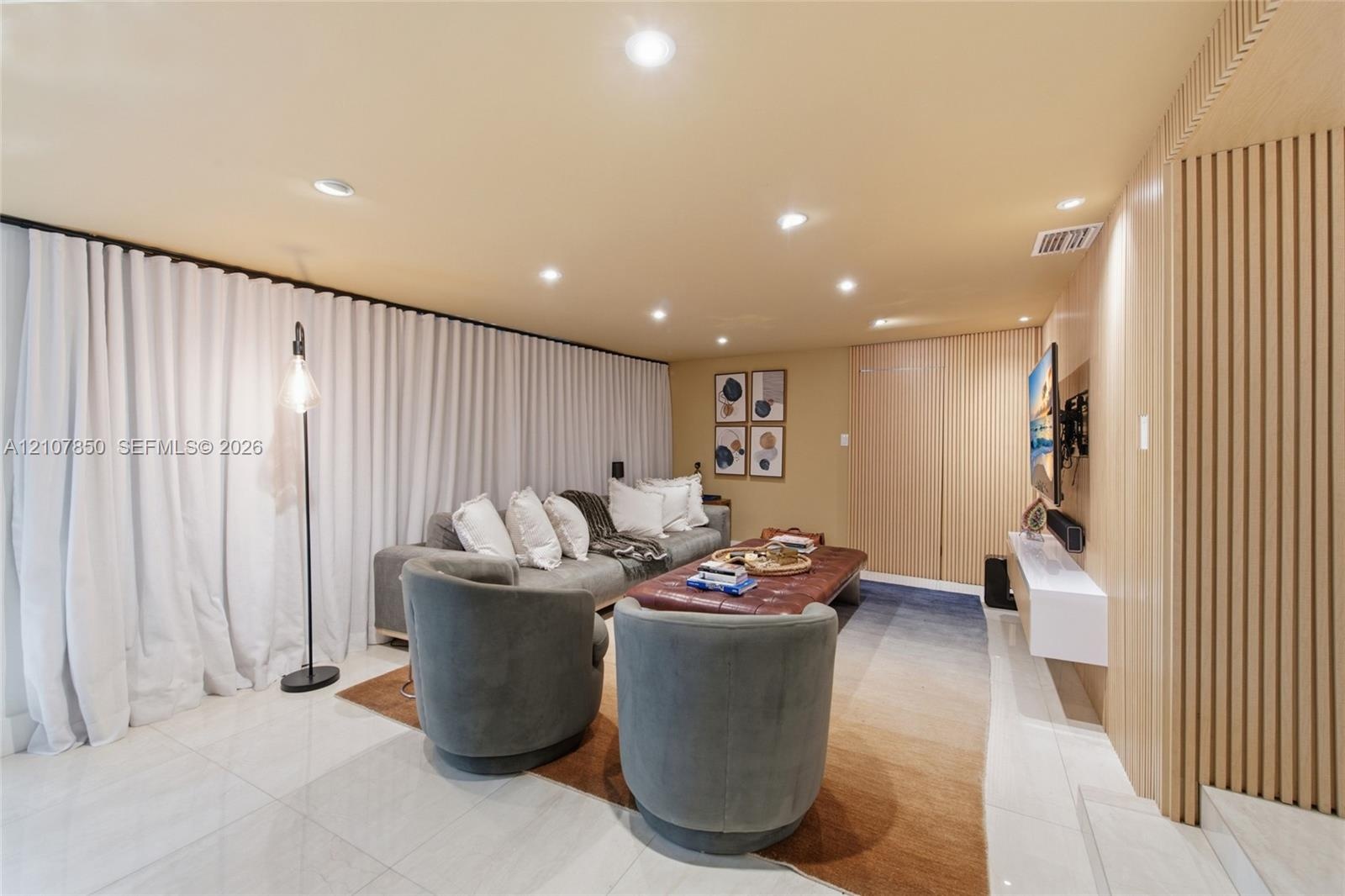 Interior space featuring large-format tile flooring, recessed ceiling lighting, a wall-mounted floating media console, and vertical wood-slat wall pan