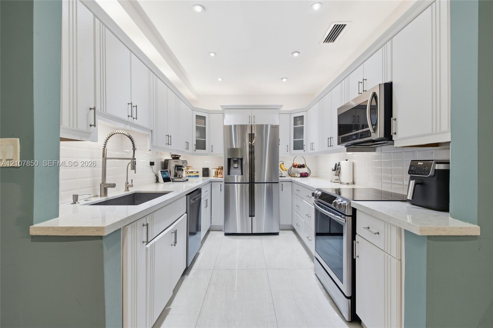 Galley kitchen featuring white cabinetry, light-toned stone-finish countertops, stainless steel appliances, a white tile backsplash, and recessed ligh