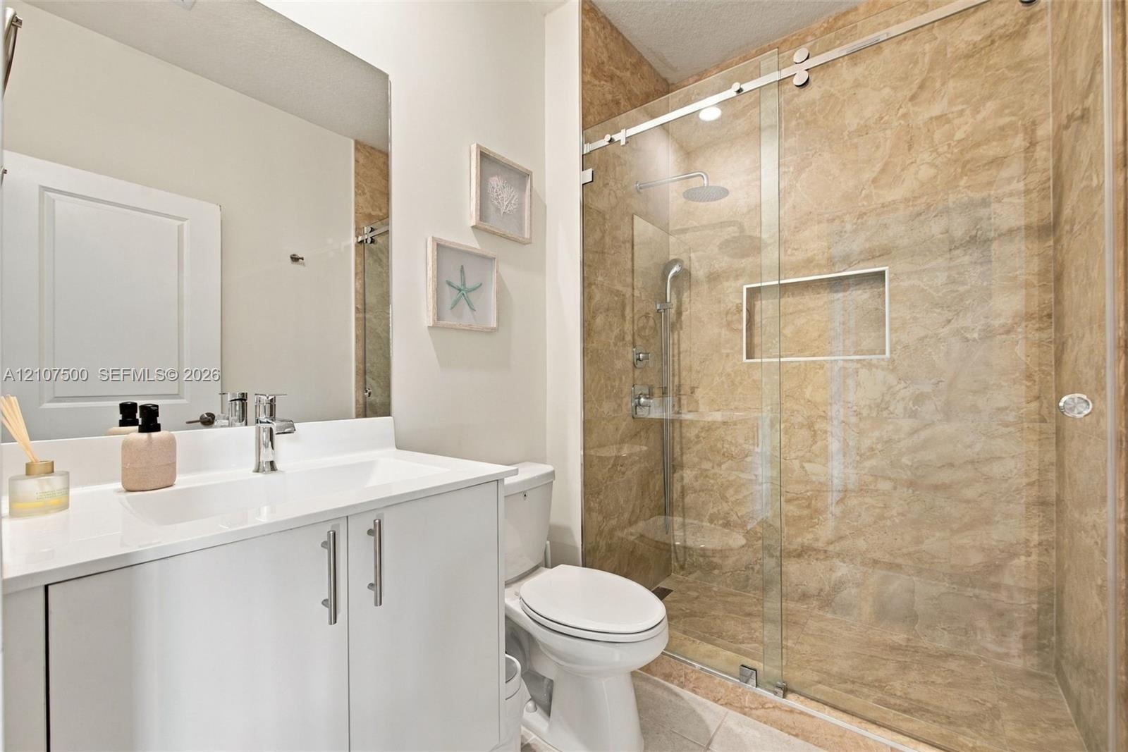 Bathroom featuring a white vanity with a rectangular sink, a frameless glass shower enclosure with sliding hardware, stone-finish wall tile, and a rec