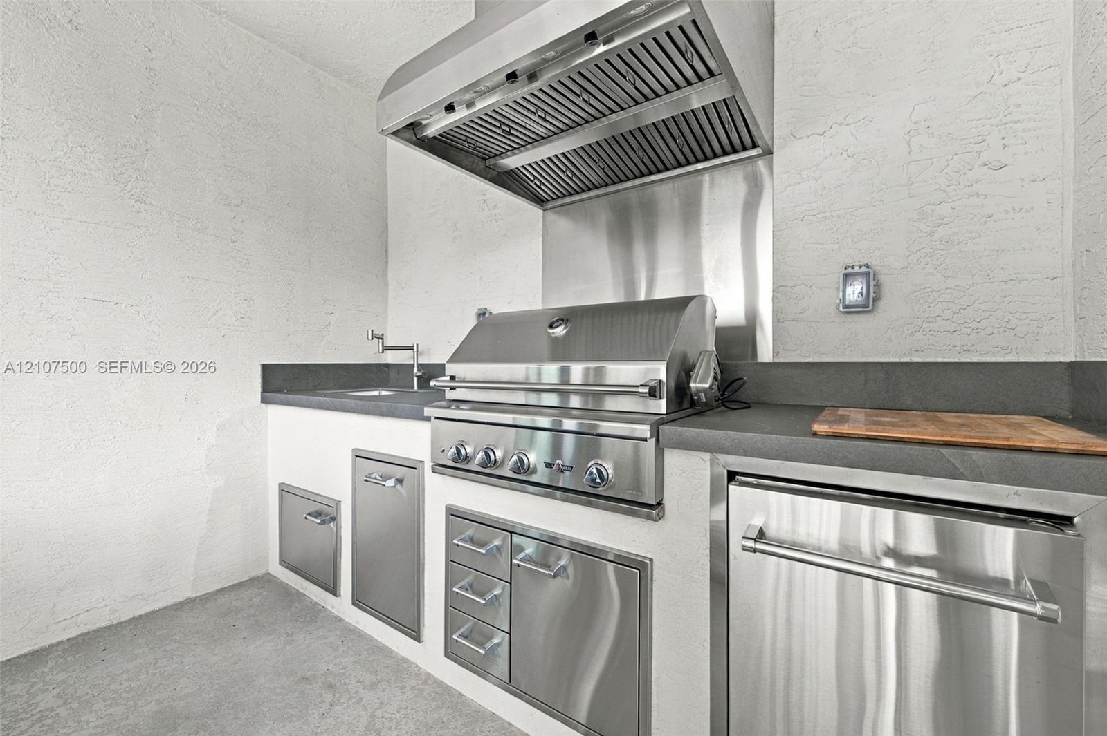 Outdoor kitchen featuring stainless steel built-in grill, professional-grade range hood, stone-finish countertops, stainless steel under-counter cabin