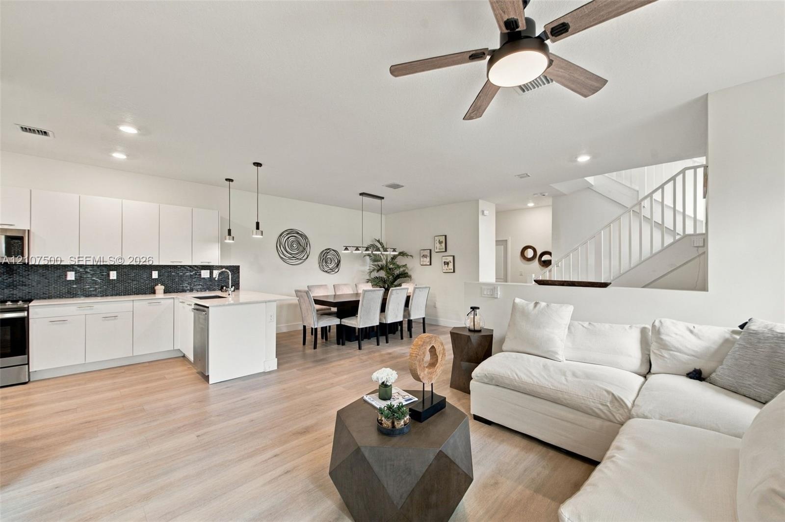 Kitchen featuring white flat-panel cabinetry, a dark tile backsplash, and a central island with countertop seating, complemented by wood-finish floori