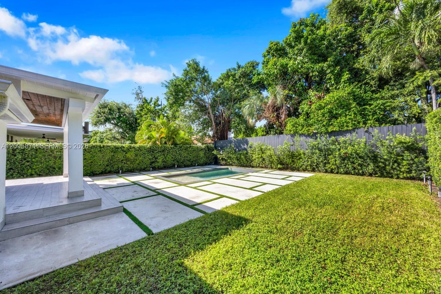 Outdoor space featuring a covered patio, rectangular pool, concrete paver decking, manicured lawn, and perimeter privacy hedging