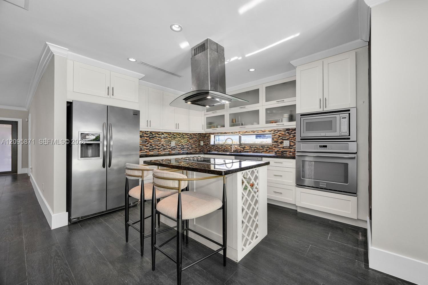 Kitchen featuring white shaker cabinetry, stainless steel appliances, dark stone countertops, a mosaic tile backsplash, and a center island with integ