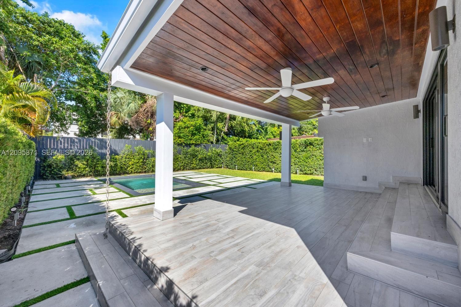 Covered patio featuring a stained wood plank ceiling, dual ceiling fans, tile flooring, and step access to the pool area with paver hardscaping