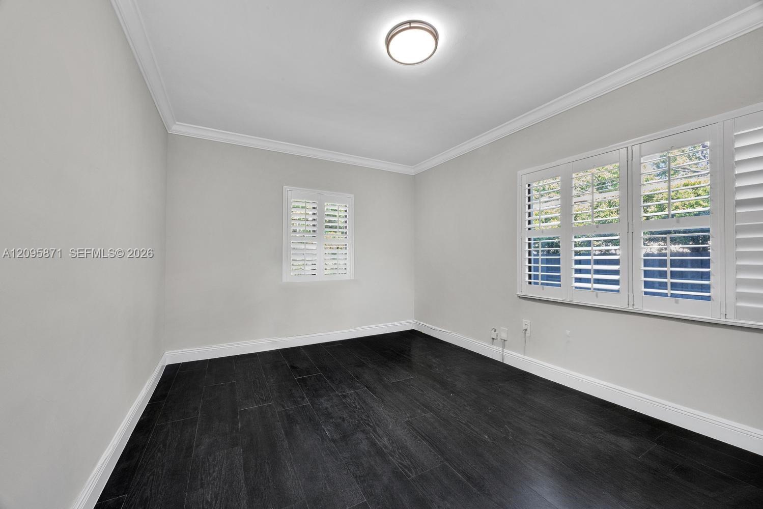 Neutral-toned interior space featuring wood-finish flooring, crown molding, and plantation shutters