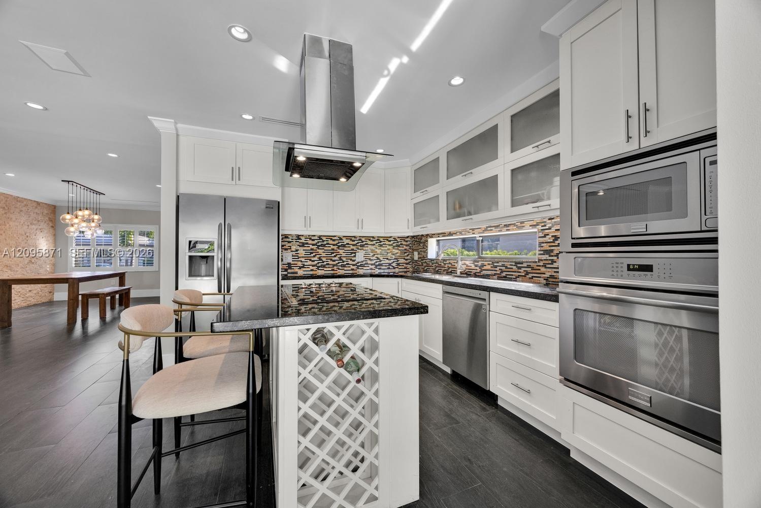 Kitchen featuring white shaker cabinetry, stainless steel appliances, built-in wine rack, stone countertops, and recessed lighting