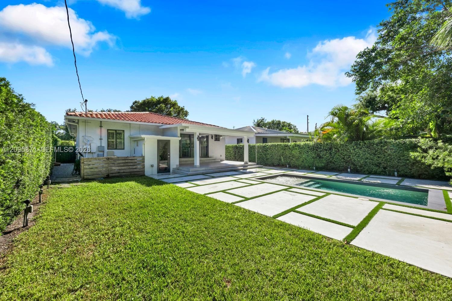 Backyard featuring a swimming pool, concrete paver patio with turf inlays, manicured lawn, and perimeter hedging
