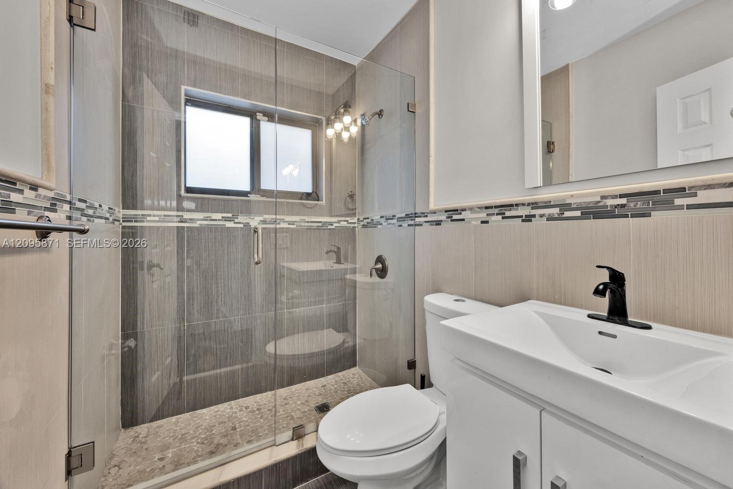 Walk-in shower with a glass enclosure, pebble-stone flooring, and decorative tile accents, paired with a white vanity featuring a rectangular basin an