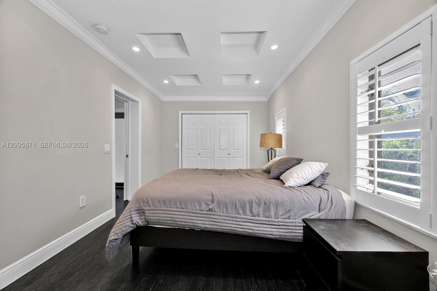 Tray ceiling with recessed lighting, dark wood-finish flooring, white plantation shutters, and double-door closet cabinetry