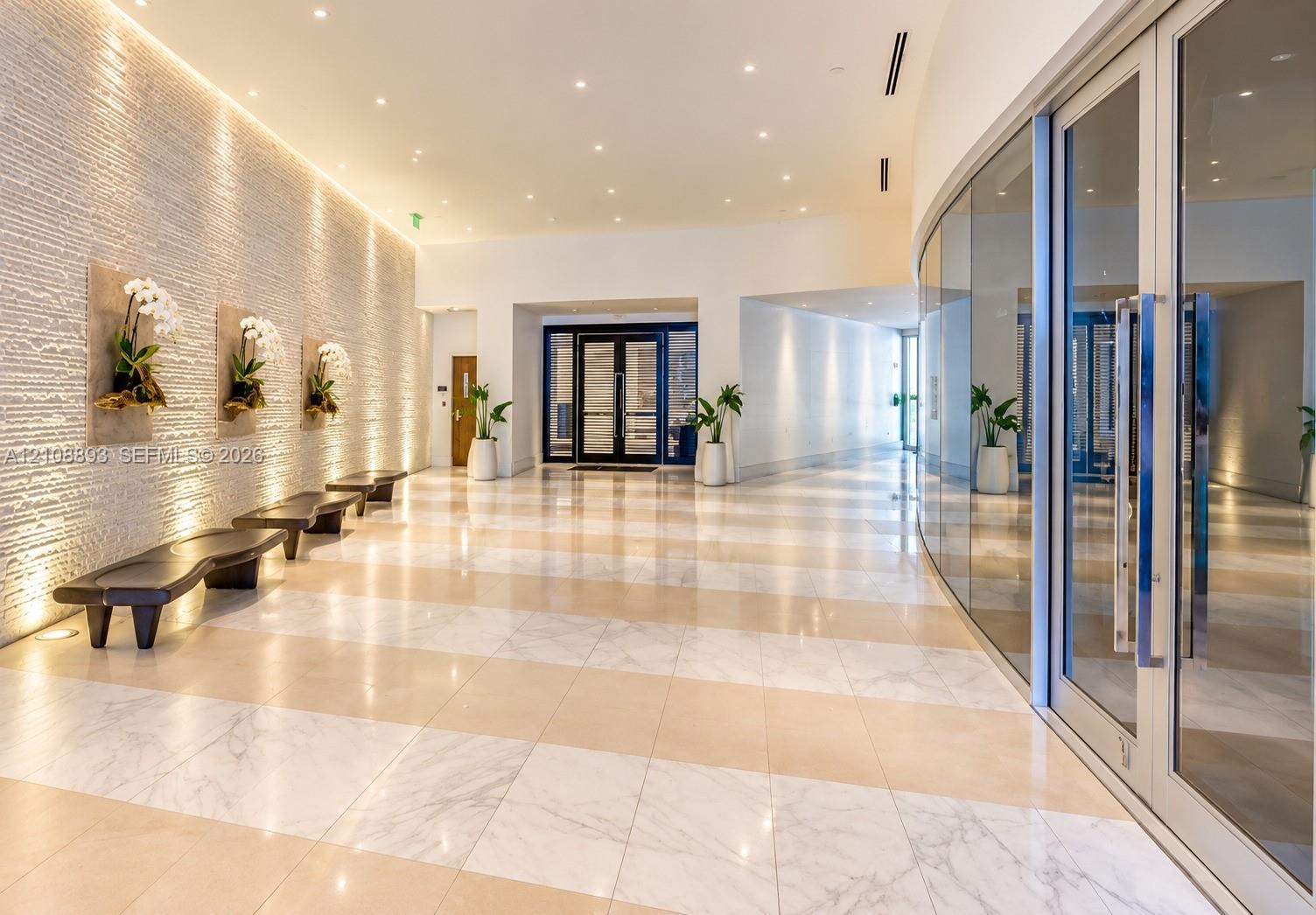 Grand lobby featuring a textured stone accent wall, large-format tile flooring, recessed ceiling lighting, and a curved floor-to-ceiling glass wall en