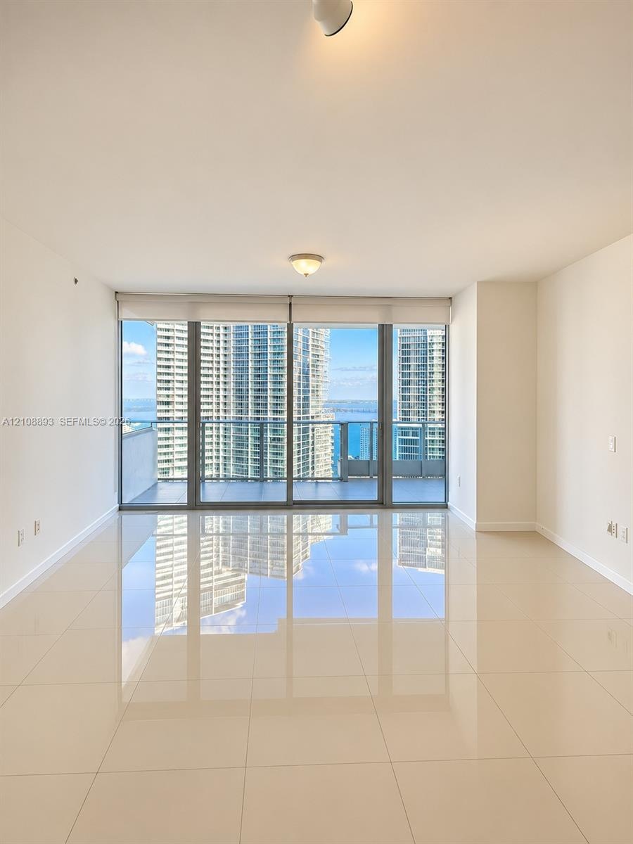 Floor-to-ceiling glass windows, ceramic tile flooring, and a glass-paneled balcony with panoramic water and skyline scenery
