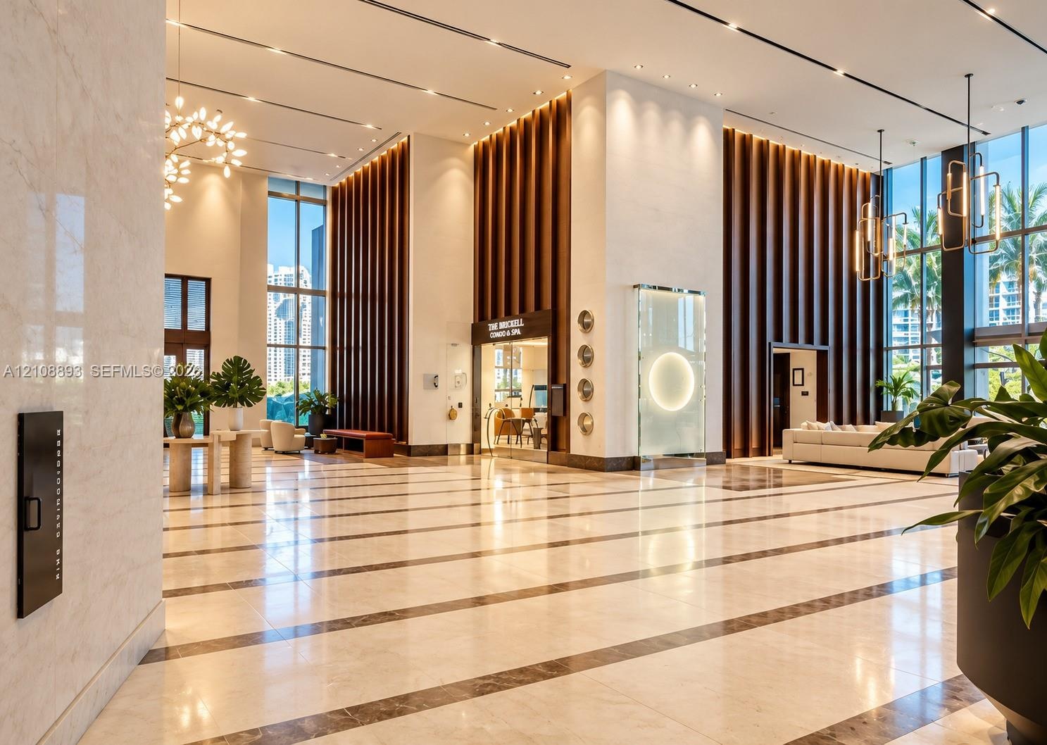 Grand lobby featuring high ceilings, floor-to-ceiling glass windows, polished stone flooring with inlaid borders, decorative vertical wood-slat wall a
