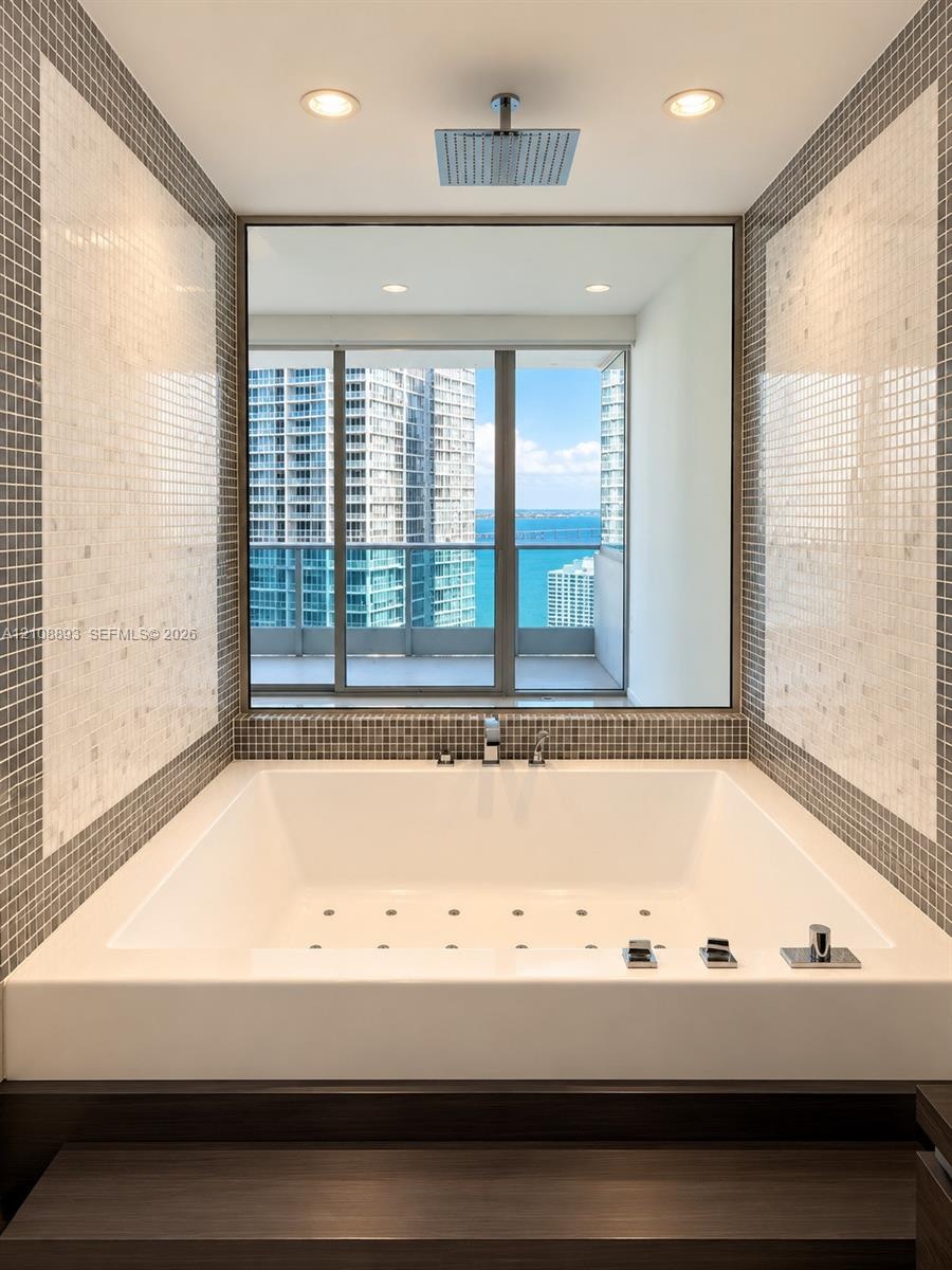 Drop-in soaking tub with a deck-mounted faucet, square rain shower head, large-format mirror, and custom mosaic tile surround