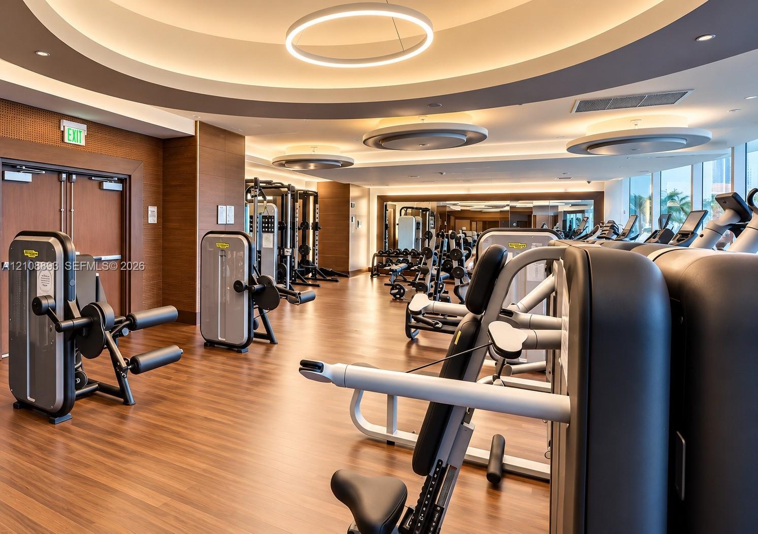 Fitness center featuring wood-finish flooring, circular recessed ceiling lighting, wall-to-wall mirrors, and floor-to-ceiling windows