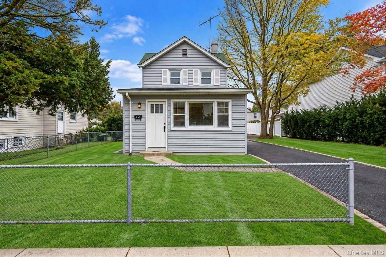 Two-story home with grey vinyl siding, white trim, a multi-pane front entry door, a paved driveway, and a chain-link fenced front yard *virtually edit