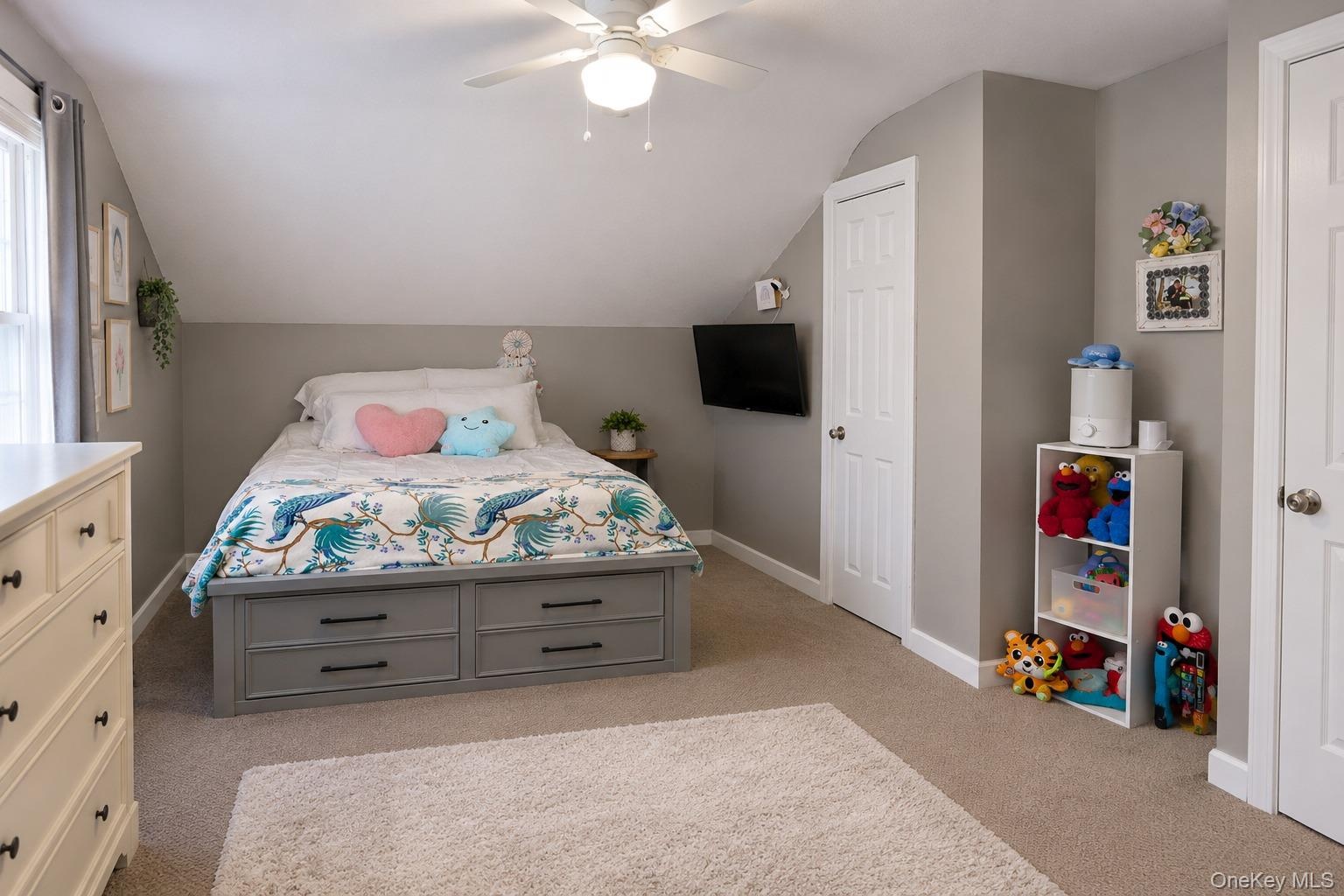 Neutral-toned bedroom featuring angled ceilings, neutral wall-to-wall carpeting, and a ceiling-mounted light fixture with integrated fan